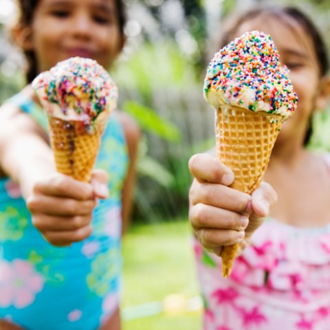 穿泳装的小女孩们分享两个洒满彩色糖果的冰淇淋甜筒的鲜艳影像